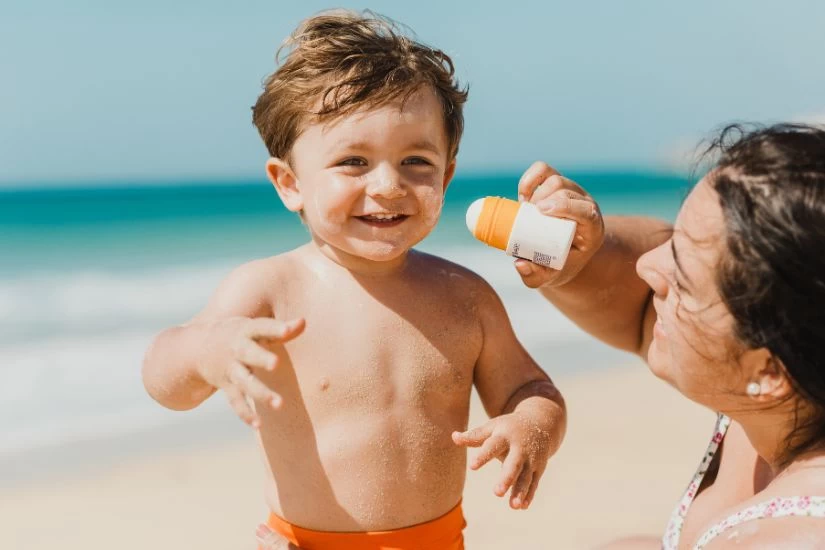 Mama nanosi detetu na lice kremu sa spf faktorom na plaži.