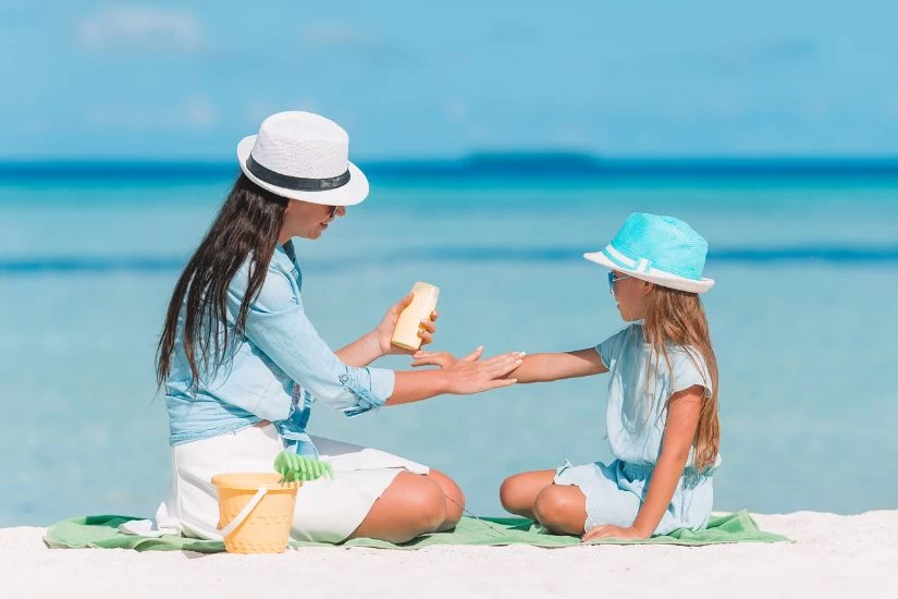 Majka i ćerka na plaži nanonose kremu za sunčanje.