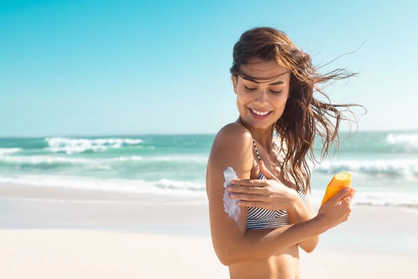 Devojka na plaži stavlja kremu na kožu.