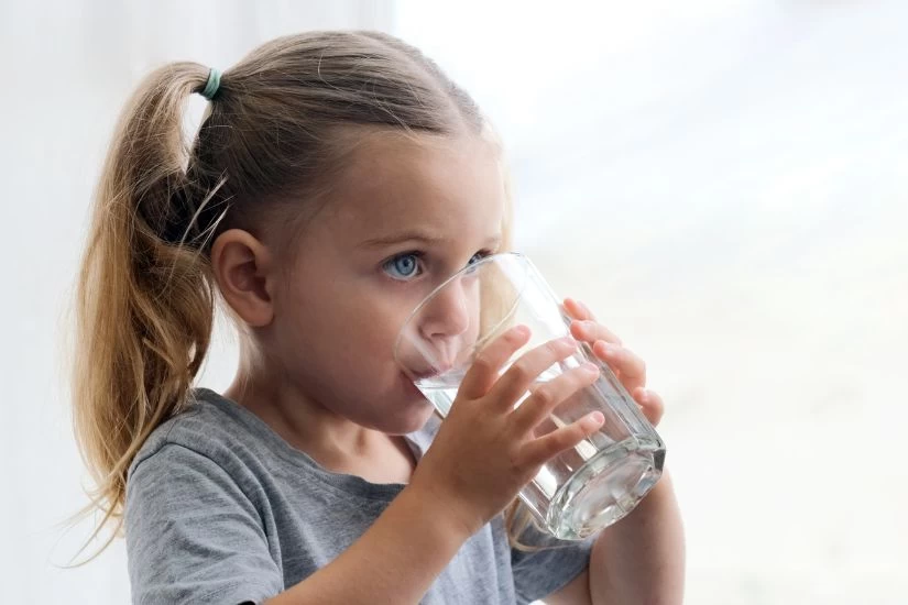 Devojčica pije vodu iz čaše.